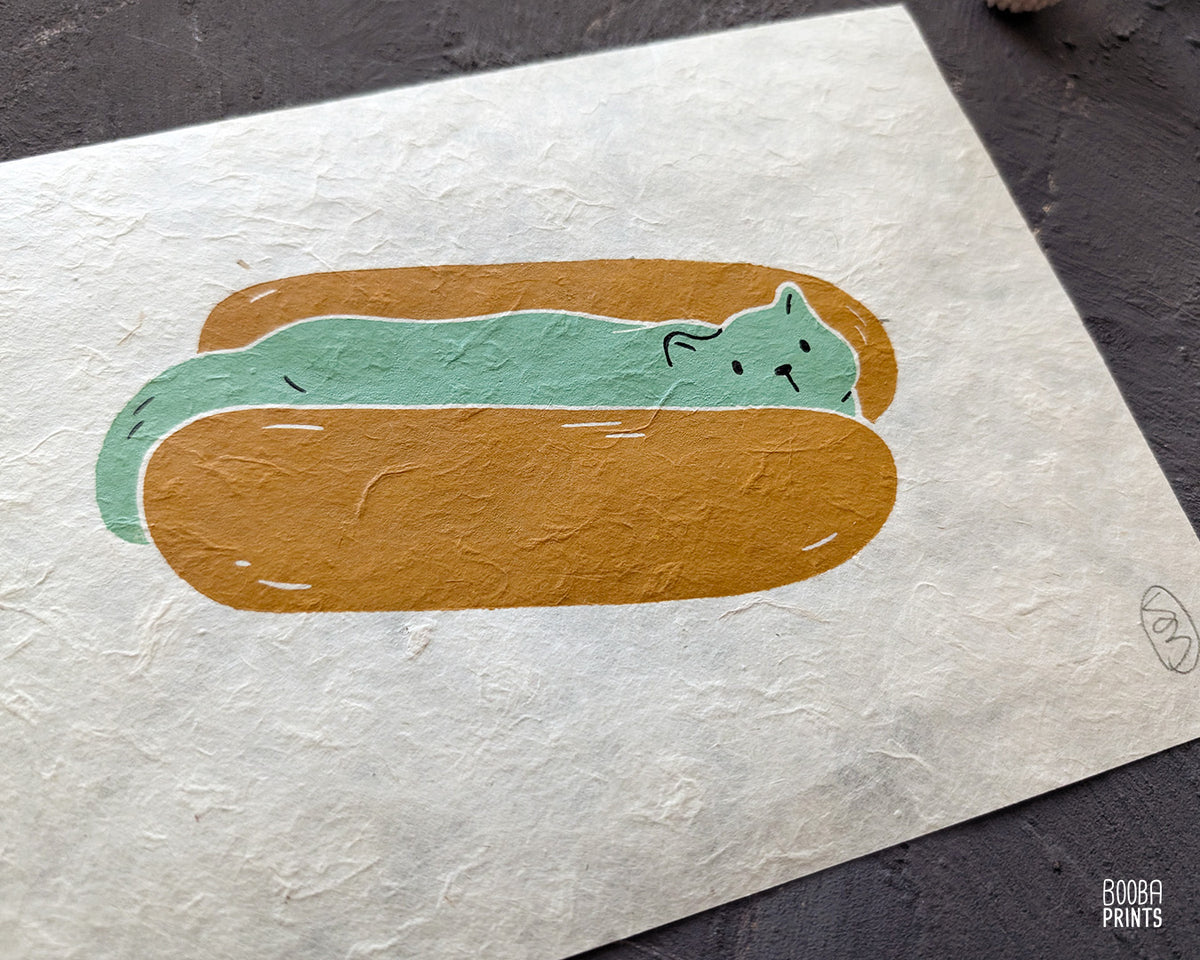 Original 2 color linocut print, printed in Ochre and mint green, showing a cute cat in a hot dog but. Cute whimsical art for your kitchen. Art by Booba Prints
