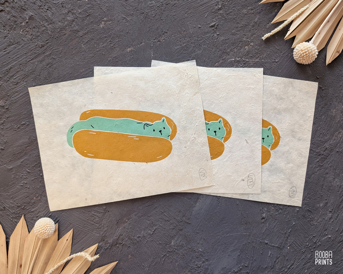 Original 2 color linocut print, printed in Ochre and mint green, showing a cute cat in a hot dog but. Cute whimsical art for your kitchen. Art by Booba Prints