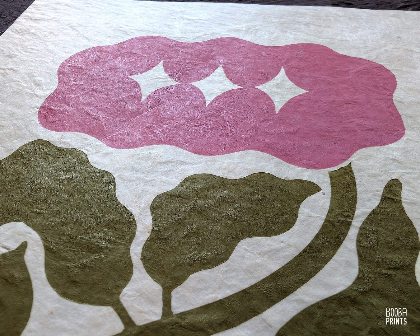 Close up of handmade linocut flower print, showing carved details and green and pink ink textures on natural Lokta paper. Art by Booba Prints