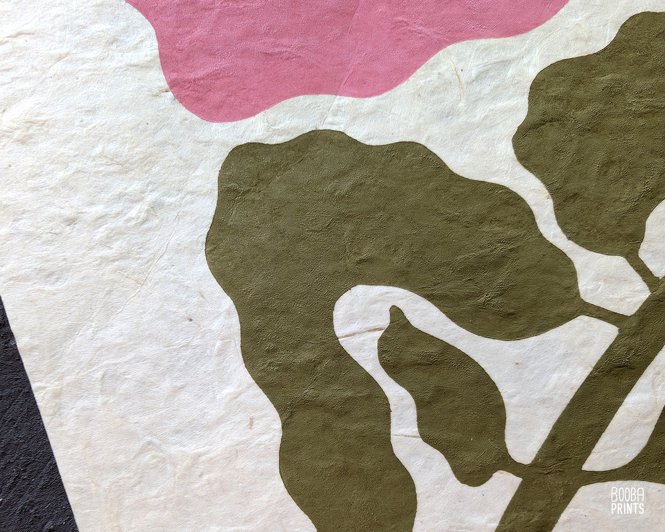 Close up of handmade linocut flower print, showing carved details and green and pink ink textures on natural Lokta paper. Art by Booba Prints