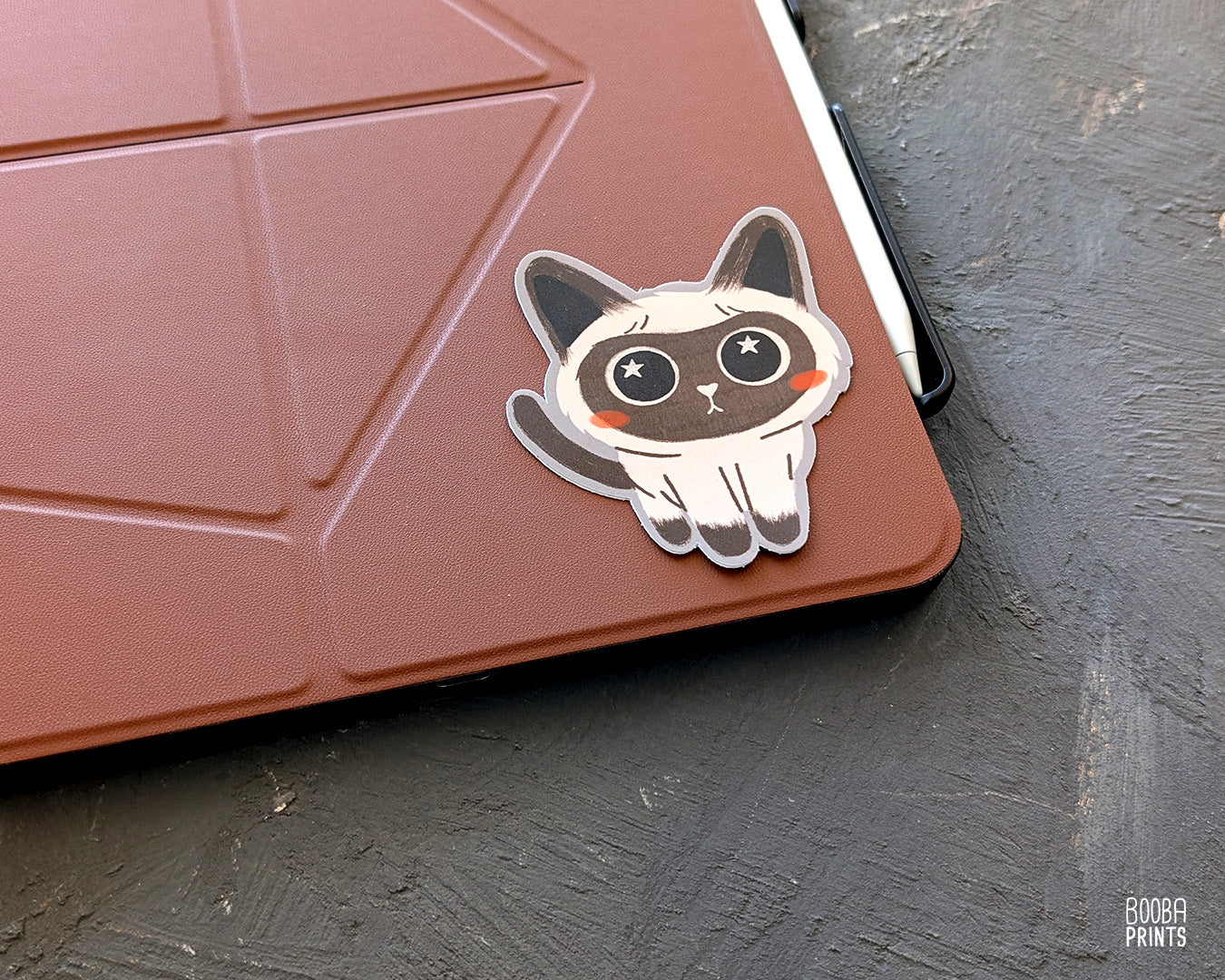 A cute stylized Siamese cat sticker on top of a tablet cover. Adorable sticker for cat lovers. Waterproof vinyl sticker for planner, bottle, laptop.