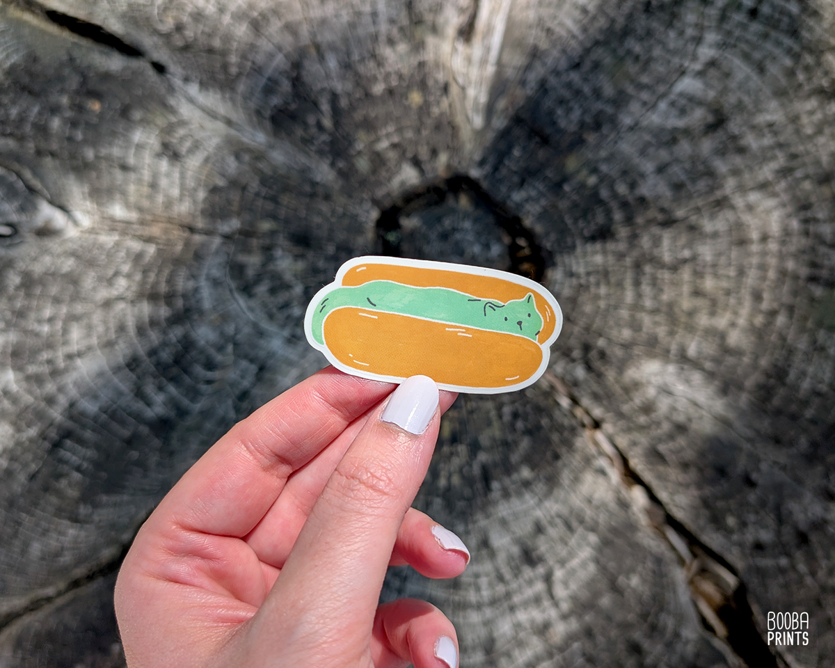 Whimsical Cat Food series, as stickers.
"Hot Dog Cat" vinyl waterproof sticker, featuring a cute green minty cat, sitting in a hot dot bun. Cute sticker for your laptop, water bottle or planner. Cute stationary sticker. Art by Booba Prints