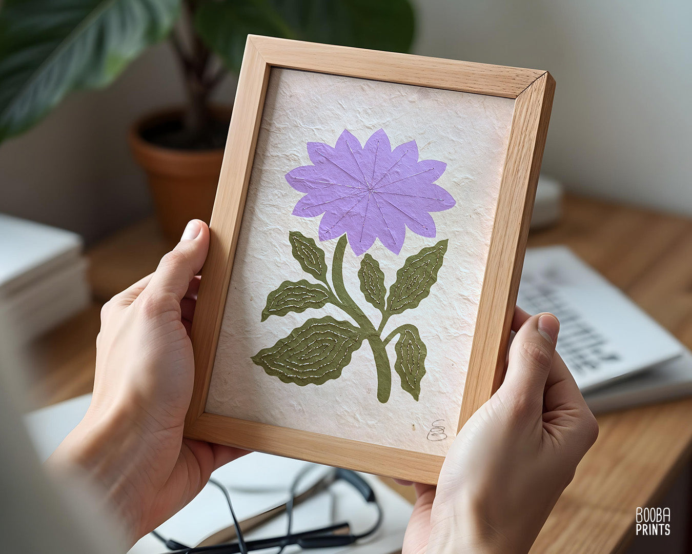 Framed artwork of a purple flower and green Flower, held by hands