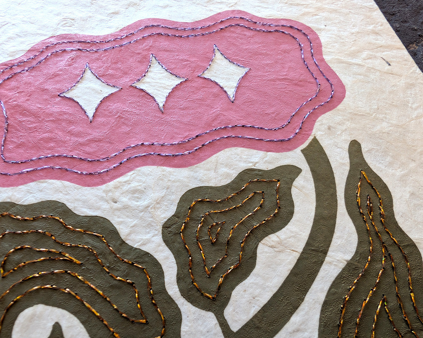 Close up on a hand printed and hand embroidered linocut print of a flower in green and pink, and embroidered in copper and lavender.