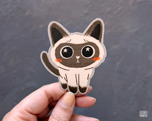 Hand holding a cute stylized Siamese cat sticker against a grey background. Adorable sticker for cat lovers. Waterproof vinyl sticker for planner, bottle, laptop. 