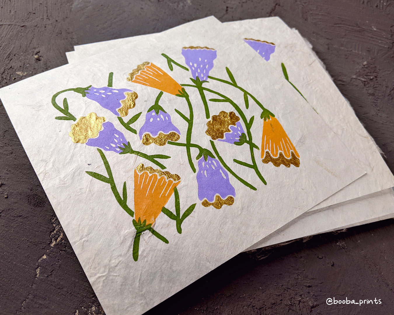 Handmade linocut print in the theme of Flora and Fauna. Floral print in 4 colors orange, purple green and gold. Printed with oil based ink and finished with metallic paint. Art by Booba Prints.